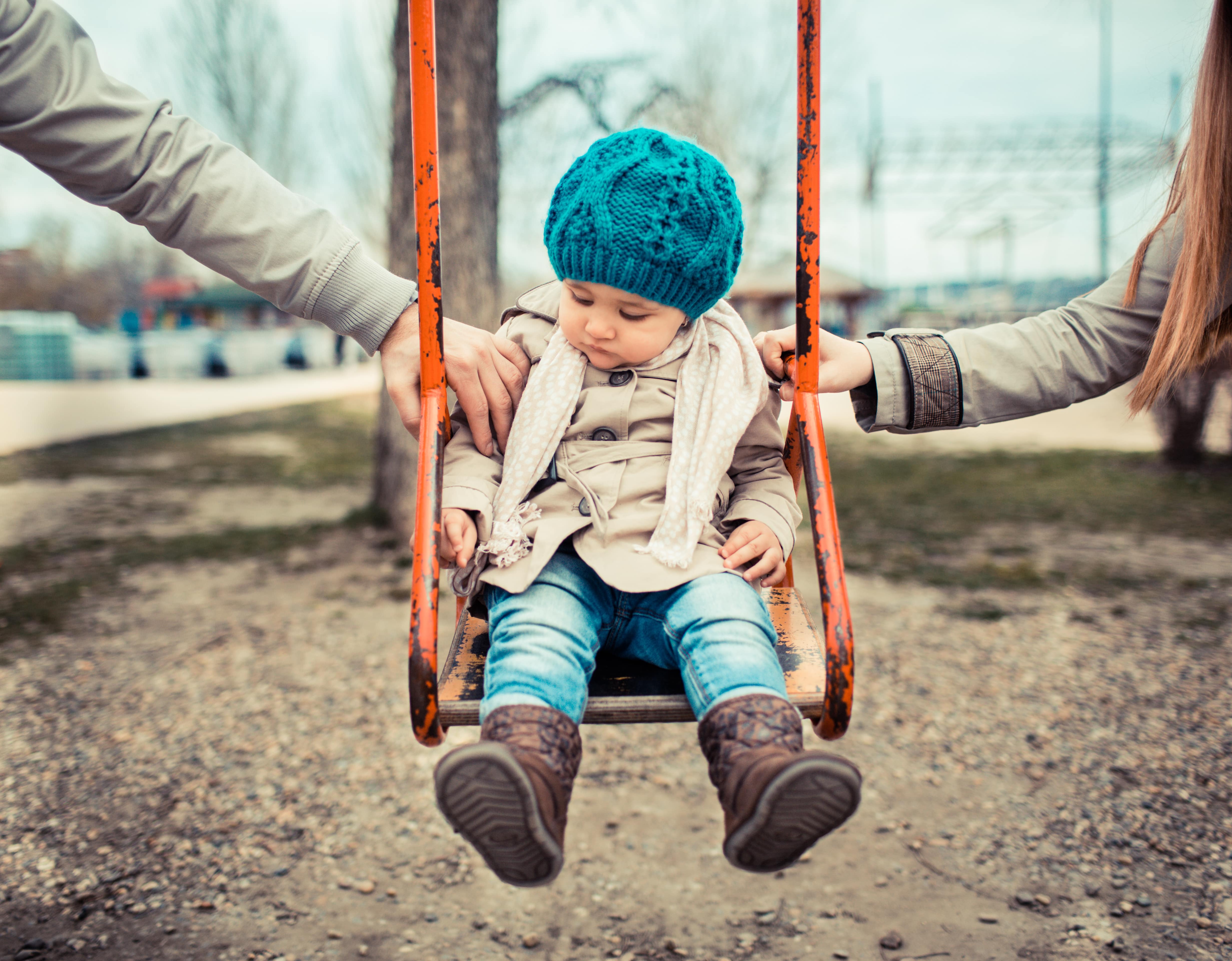 Parents swinging child on swing while working through child custody.