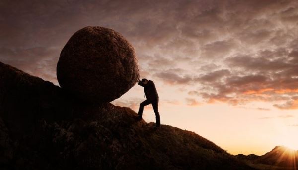 Man pushing a large boulder uphill